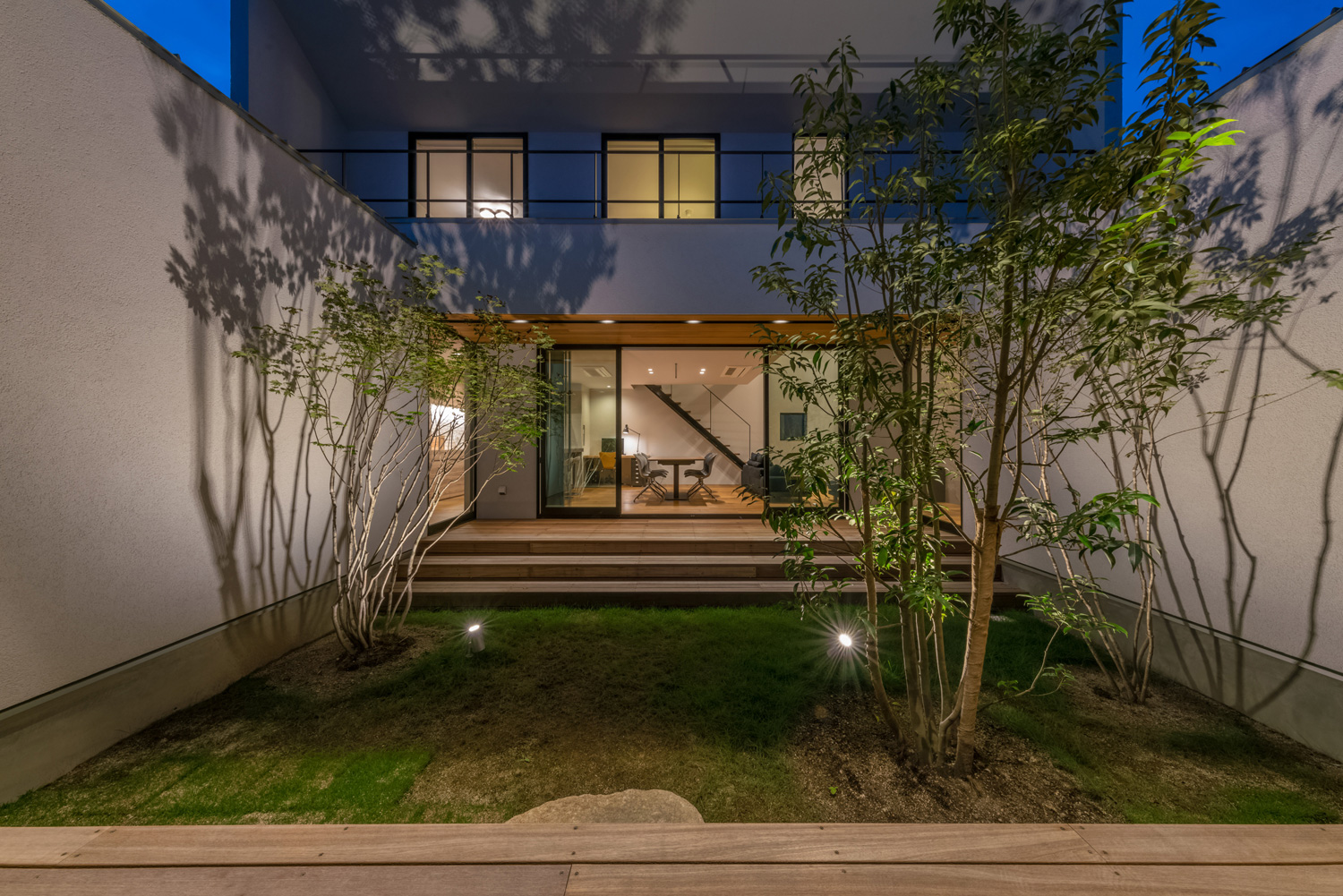 シンボルツリーがライトアップされた中庭越しにLDKが見える様子・デザイン住宅 注文住宅・デザイン住宅建築実例_『CASE576 回廊の家』_中庭