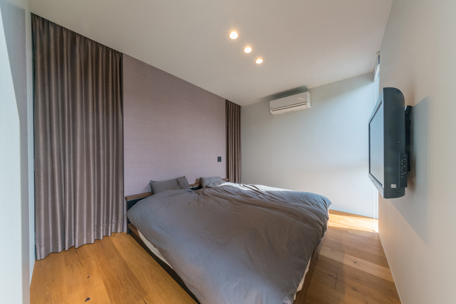 壁にテレビを取り付けたグレーのベッドを置いた寝室・デザイン住宅 注文住宅・デザイン住宅建築実例_『CASE576 回廊の家』_寝室