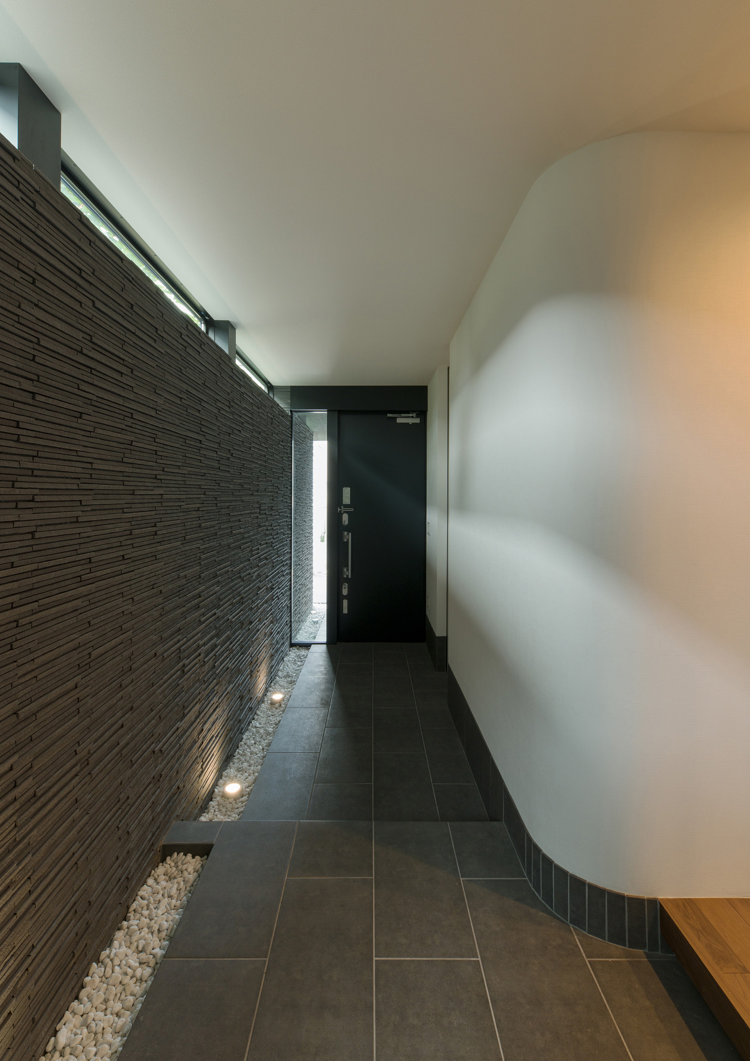 石の壁や壁際に敷石があるタイルの玄関・デザイン住宅 注文住宅・デザイン住宅建築実例_『CASE577 紬(つむぎ)の家』_玄関