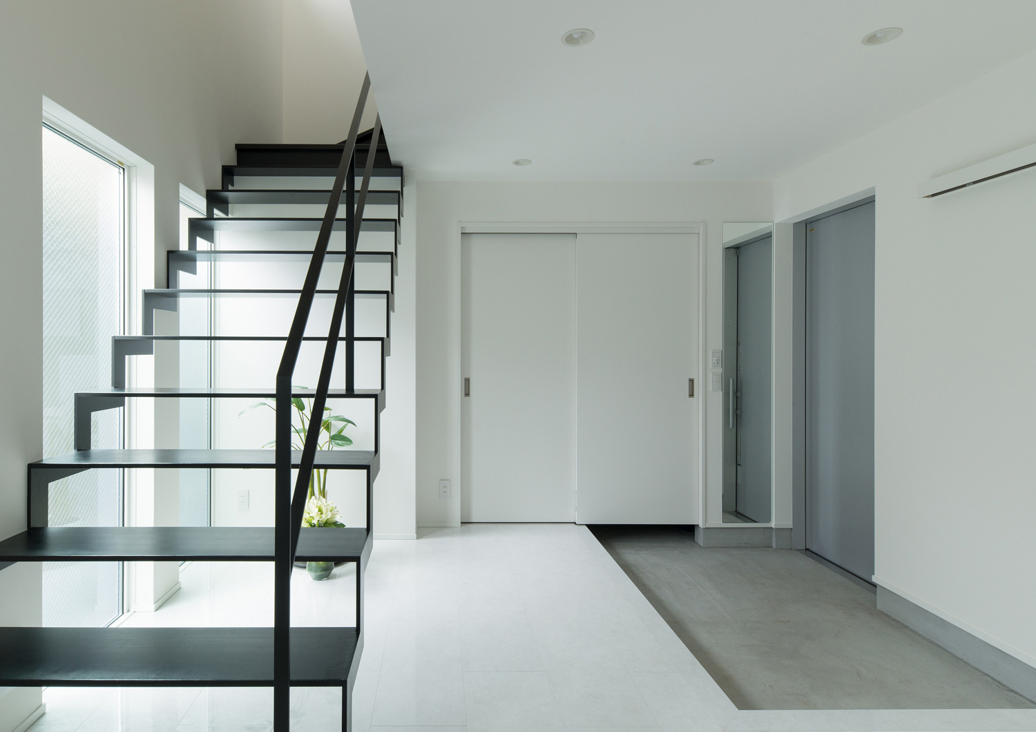 モルタルの玄関の正面にある、黒いアイアンのスケルトン階段・デザイン住宅 注文住宅・デザイン住宅建築実例_『CASE579 Functional House』_玄関