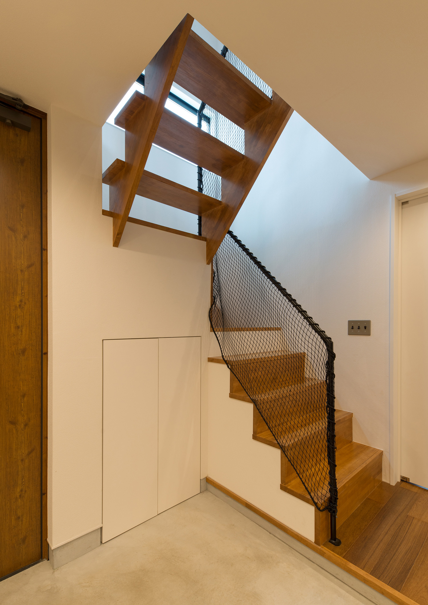 モルタルの玄関のそばにあるネット付きの木製の箱型階段・デザイン住宅 注文住宅・デザイン住宅建築実例_『CASE582 大切な時を刻む家』_階段