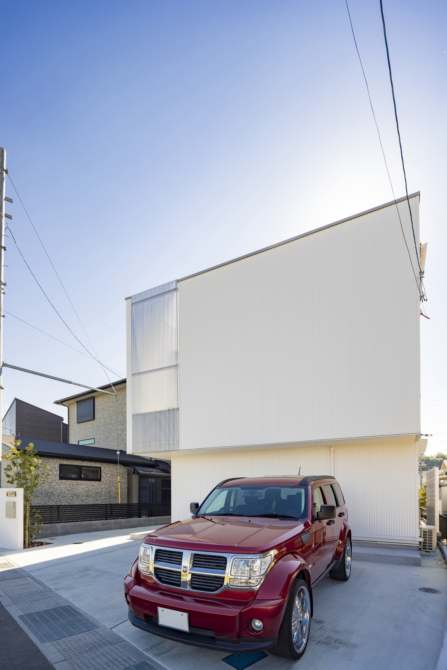 白いガルバリウム鋼板の外壁の家の前に赤い車が一台止まっている様子・デザイン住宅 注文住宅・デザイン住宅建築実例_『CASE598 爽 ~風と光~』_外観