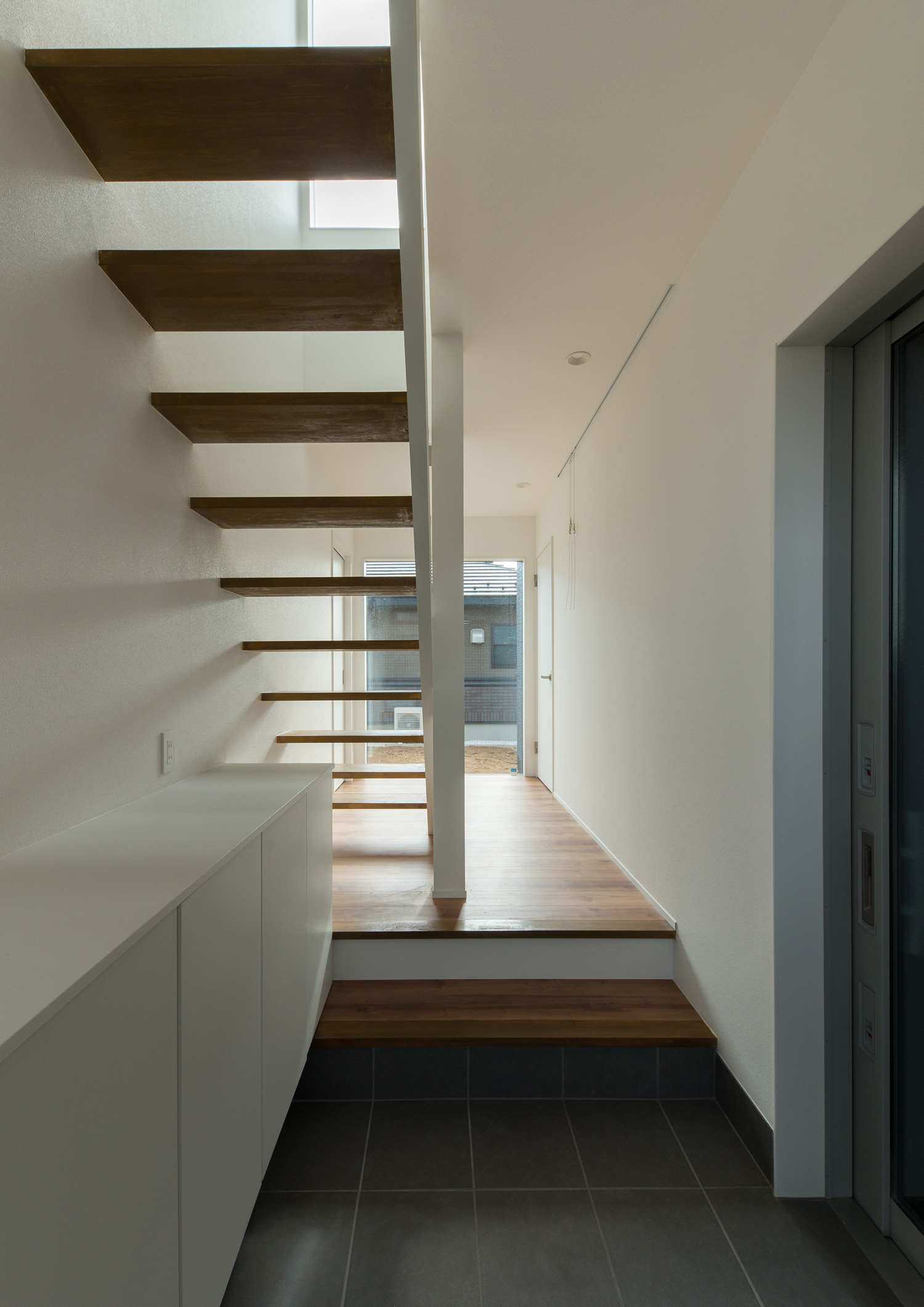 正面に窓がある、スケルトン階段が横切る玄関・デザイン住宅 注文住宅・デザイン住宅建築実例_『CASE611 黒曜×石英』_玄関