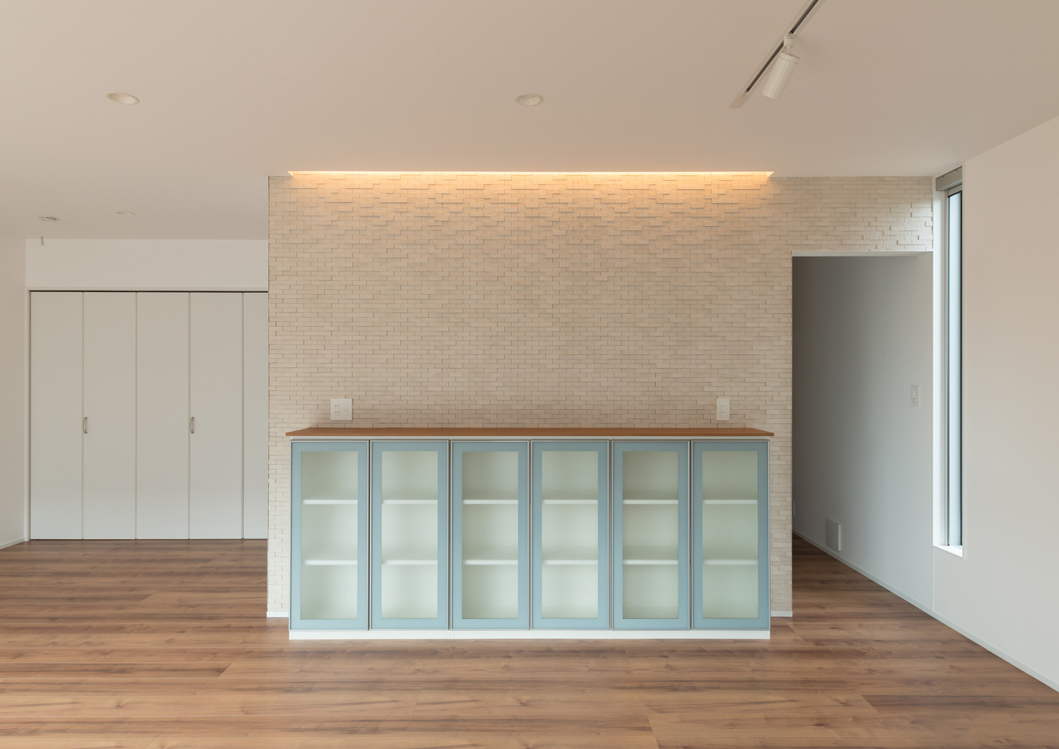 タイルのアクセントウォール部分に間接照明を取り付け、ガラス扉付きのキャビネットを置いたLDK・デザイン住宅 注文住宅・デザイン住宅建築実例_『CASE611 黒曜×石英』_LDK