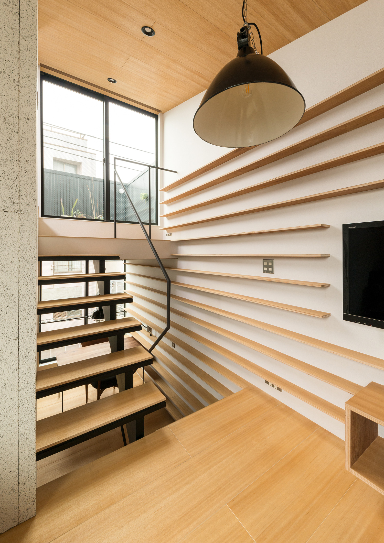ペンダントライトが吊り下げられた、壁一面に木製の棚を設けたスキップフロアのLDK・デザイン住宅 注文住宅・デザイン住宅建築実例_『CASE612 たなのいえ』_LDK
