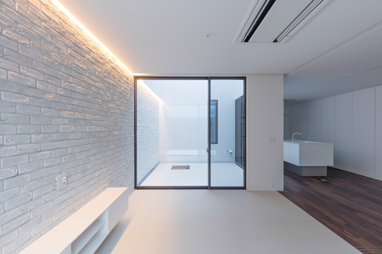 白いタイルのアクセントウォールに間接照明が取り付けられた、中庭に繋がる窓のあるLDK・デザイン住宅 注文住宅・デザイン住宅建築実例_『CASE616 HOUSE.FLOAT』_LDK