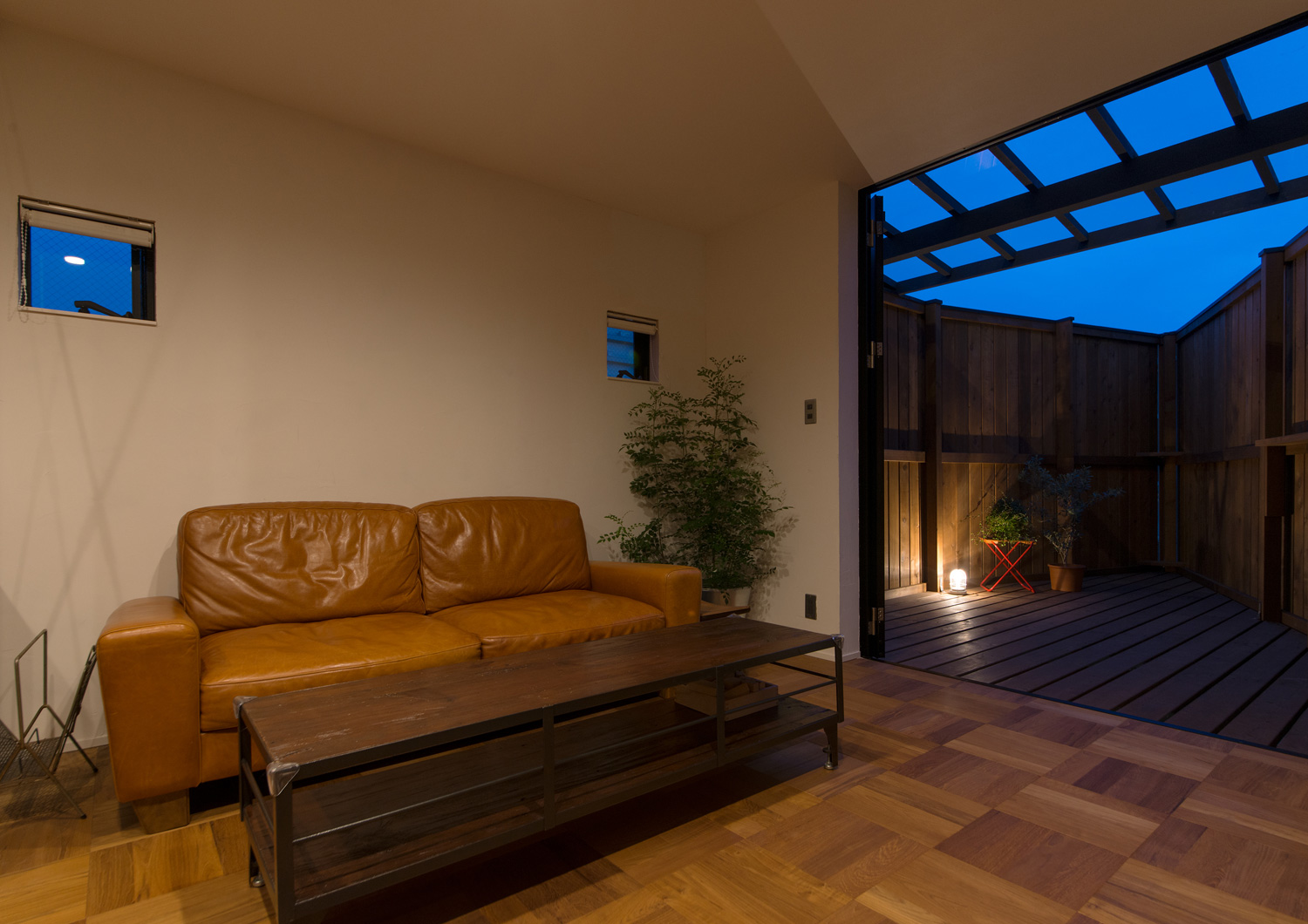 ソファーを置いたLDKから間接照明が置かれたウッドデッキのバルコニーを見た様子・デザイン住宅 注文住宅・デザイン住宅建築実例_『CASE626 Triangle』_LDK