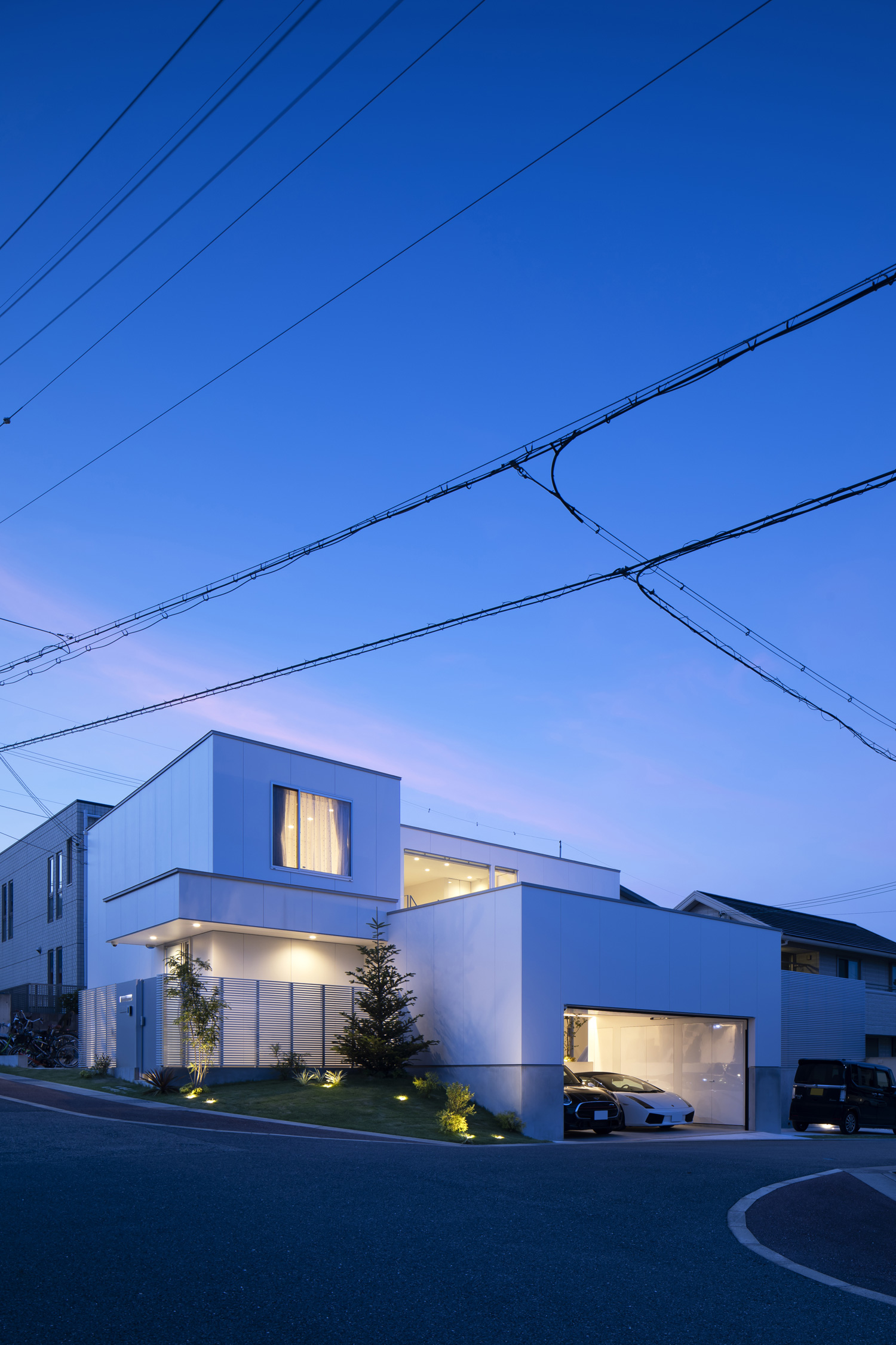 ガレージや窓から光が漏れる、角地に建つ住宅を遠くから見た様子・デザイン住宅 注文住宅・デザイン住宅建築実例_『CASE627 HOUSE . GARAGE HOUSE』_外観