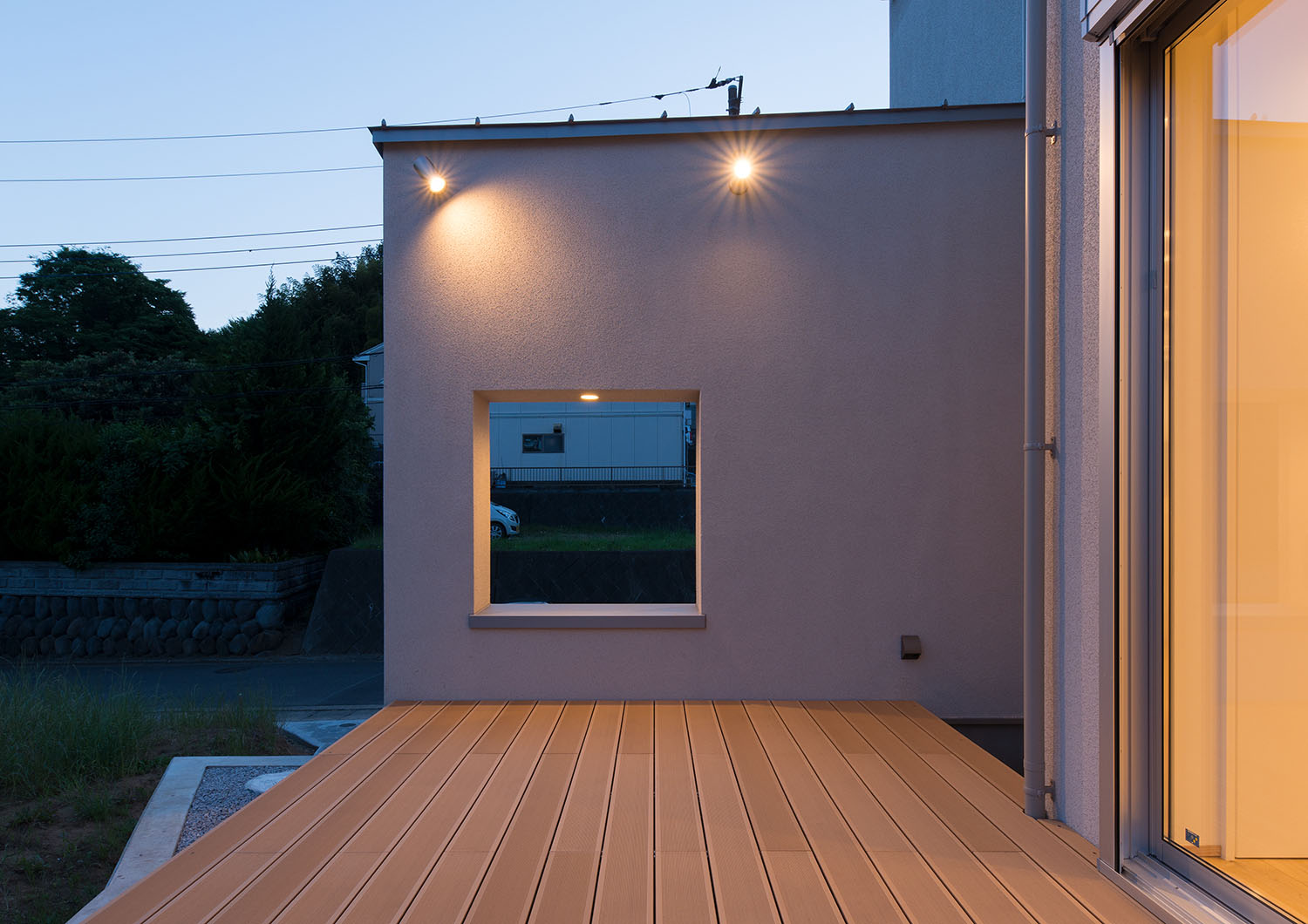 ウッドデッキのテラスを隠すように設けられた壁が照明に照らされる様子・デザイン住宅 注文住宅・デザイン住宅建築実例_『CASE550 three box house』_テラス・バルコニー