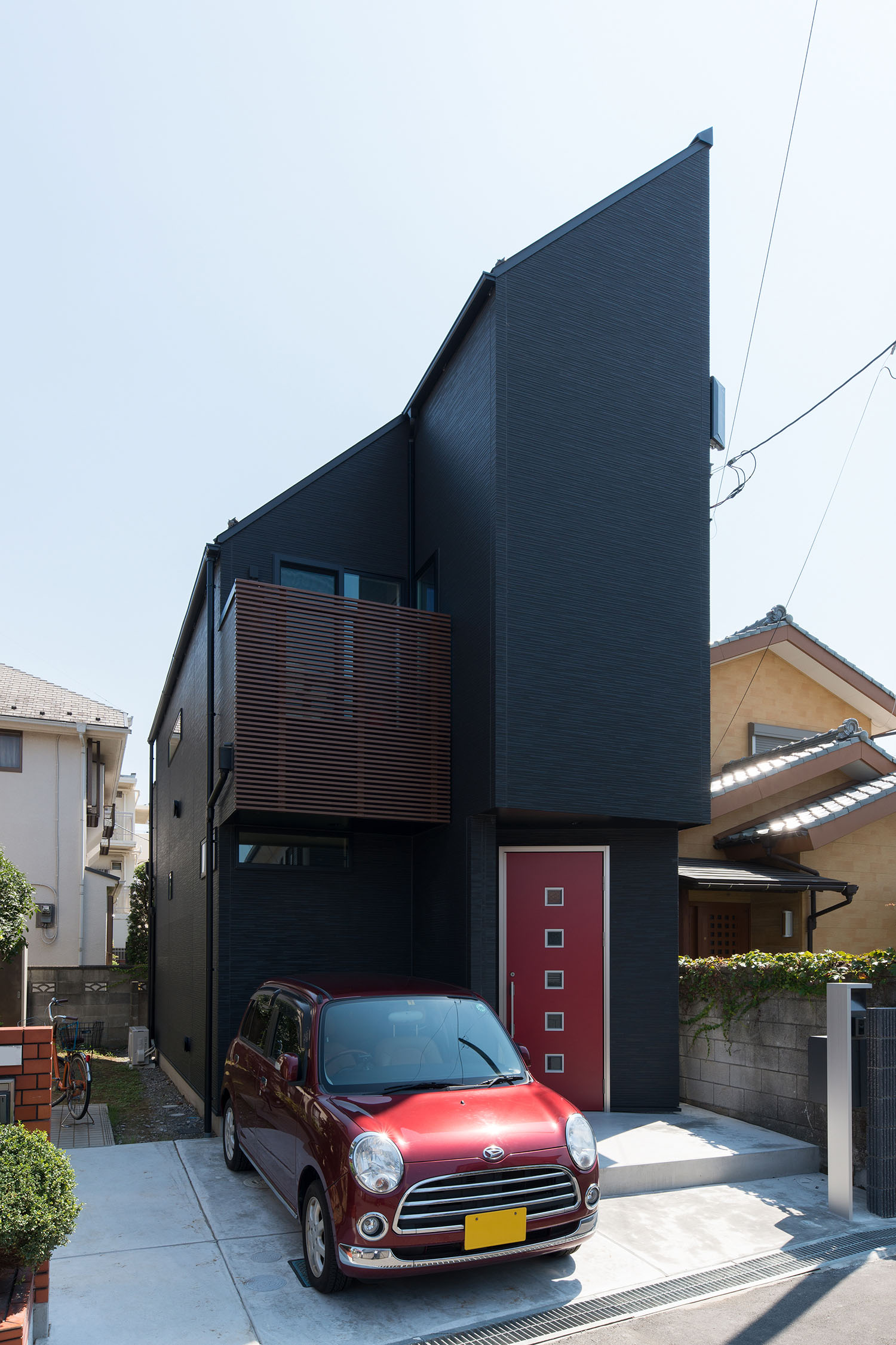 赤い玄関扉が付いた黒い斜め屋根の家の前に赤い軽自動車が一台止まっている様子・デザイン住宅 注文住宅・デザイン住宅建築実例_『CASE594 TOOL BOX』_外観
