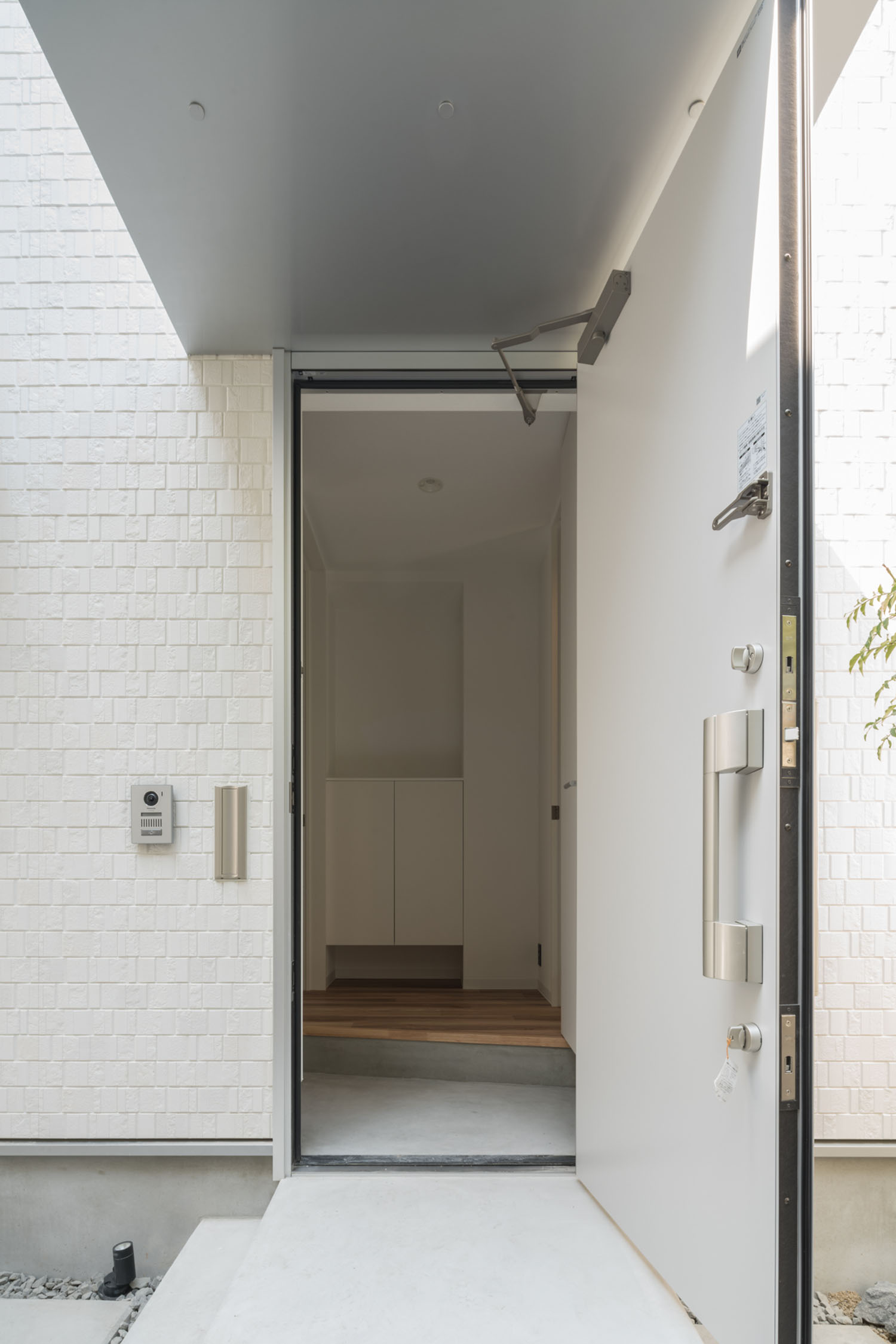 白い玄関扉が開けられ、モルタルの玄関が見える様子・デザイン住宅 注文住宅・デザイン住宅建築実例_『CASE623 HOUSest-Life+Cafe』_玄関