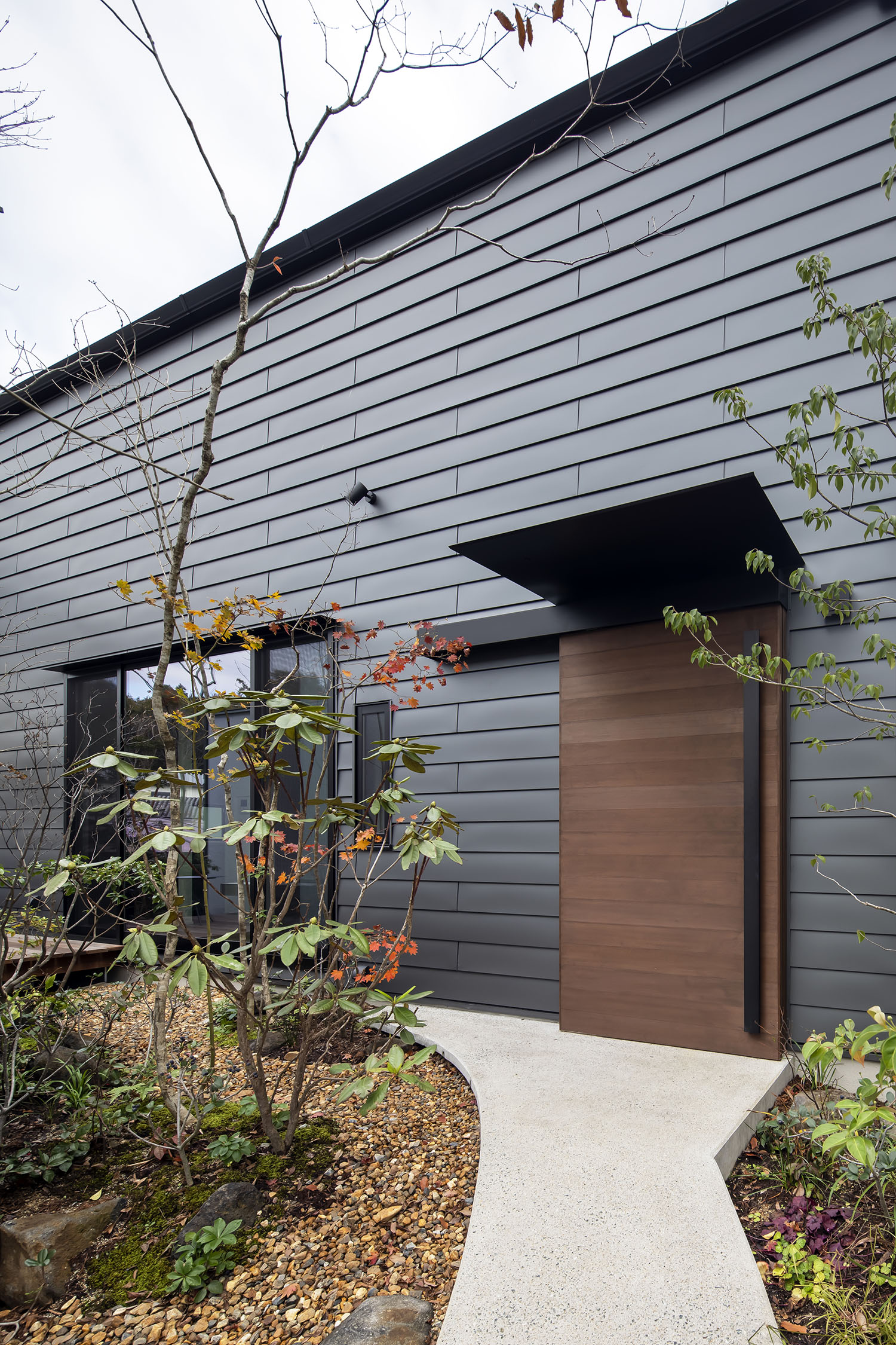 黒い外壁に木の扉がついた住宅の回りに植栽がある様子・デザイン住宅 注文住宅・デザイン住宅建築実例_『CASE698 「景の家」』_外観