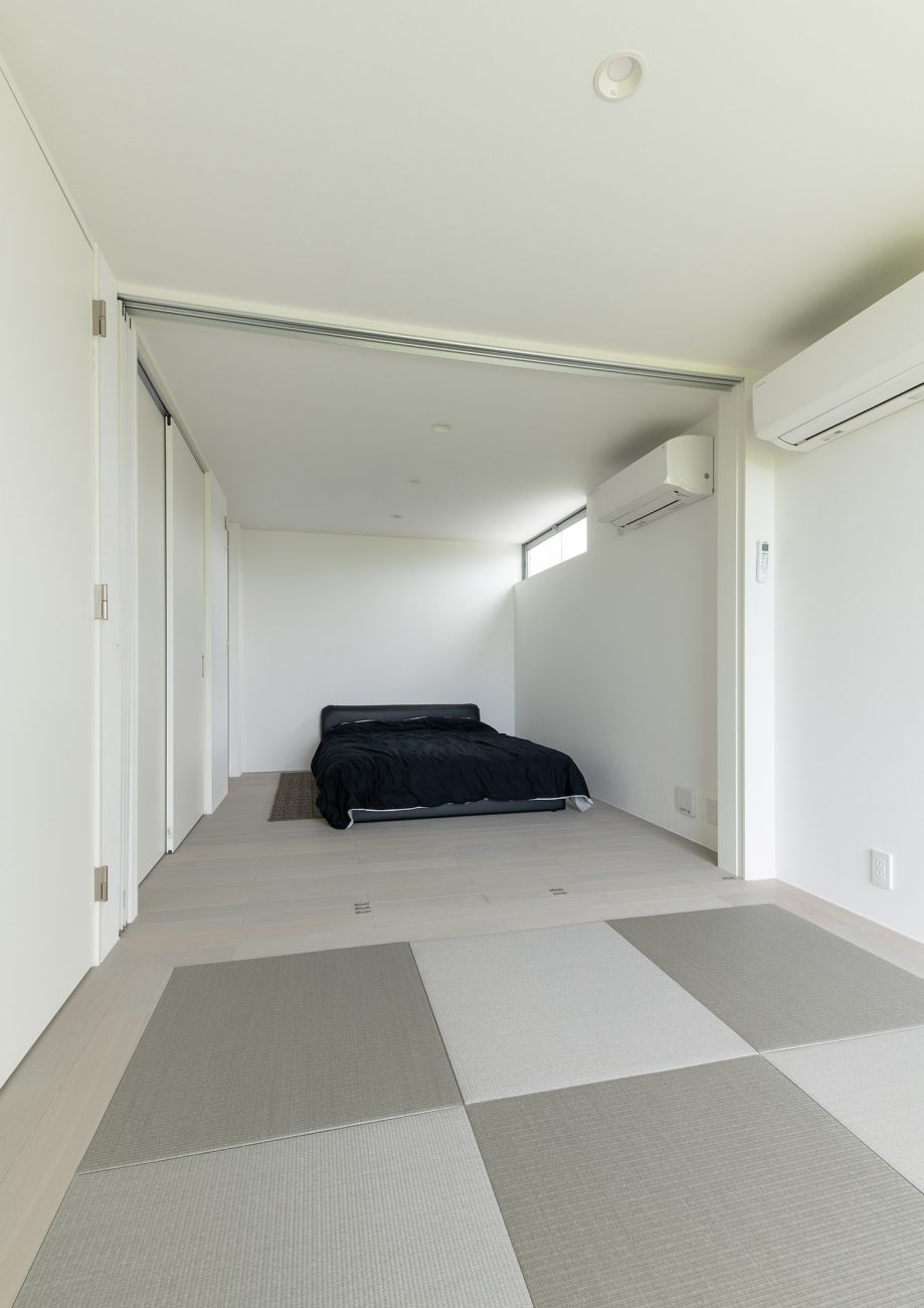 琉球畳を敷いた和室と黒いベッドのある寝室が引き戸で仕切られている様子・デザイン住宅 注文住宅・デザイン住宅建築実例_『CASE750 WHITE GATE』_和室